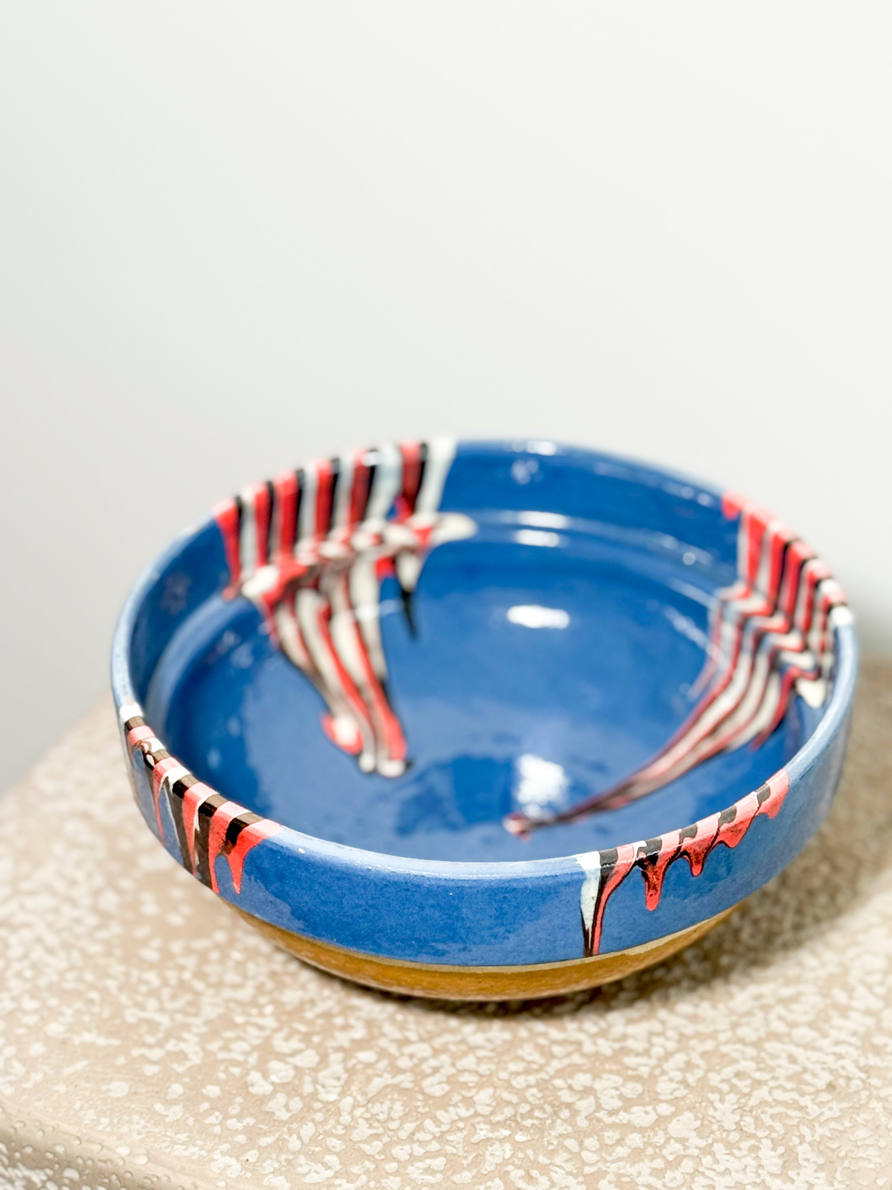 Ceramic bowl with blue glaze and red and black abstract patterns on a textured surface.