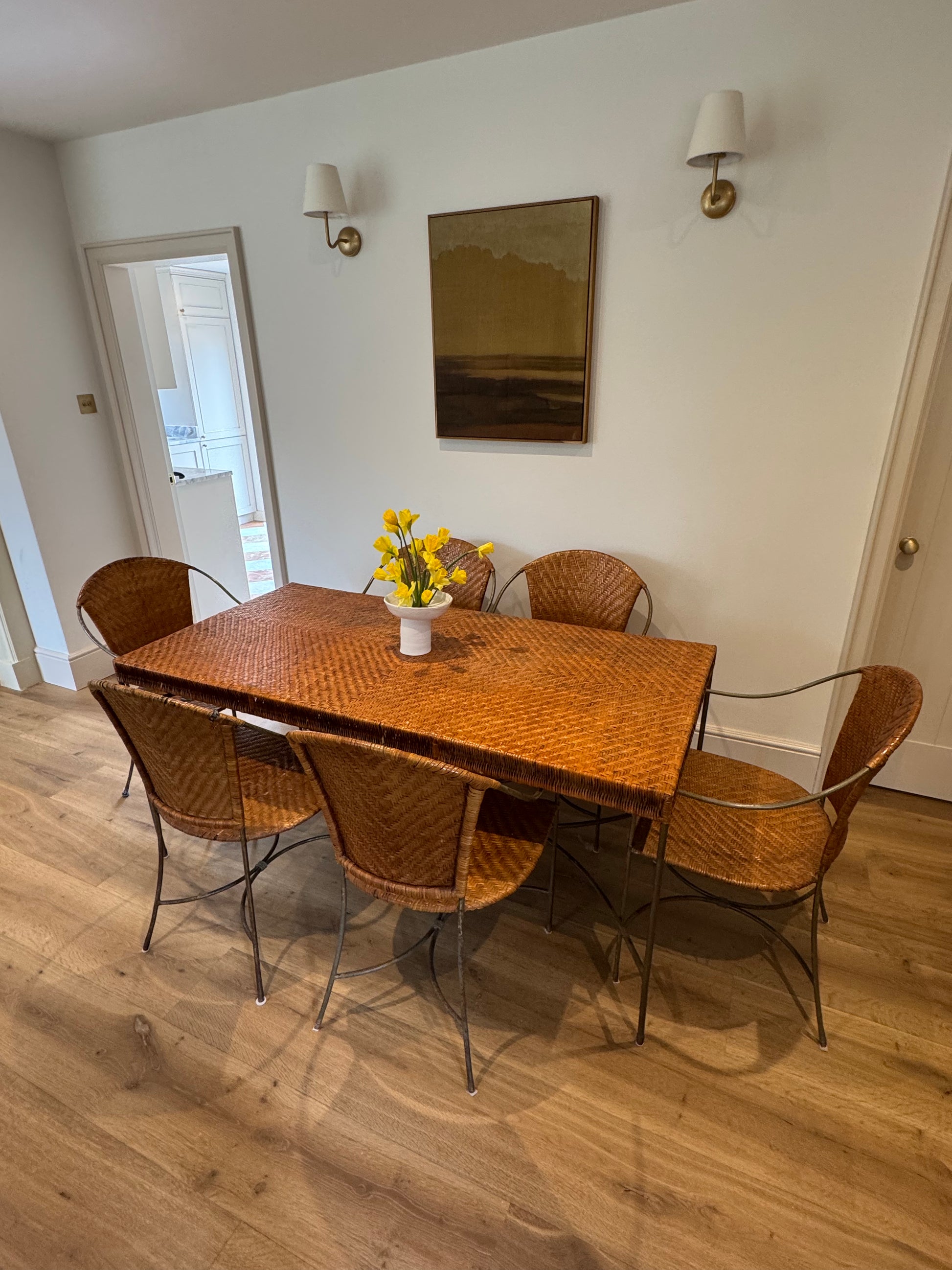 A beautifully proportioned woven rattan dining set, combining warmth, texture and sculptural metalwork in perfect balance. The rectangular table features a tightly woven herringbone rattan top in a rich honeyed tone, framed by slender dark metal legs with elegant stretchers that give the piece a light, architectural feel.