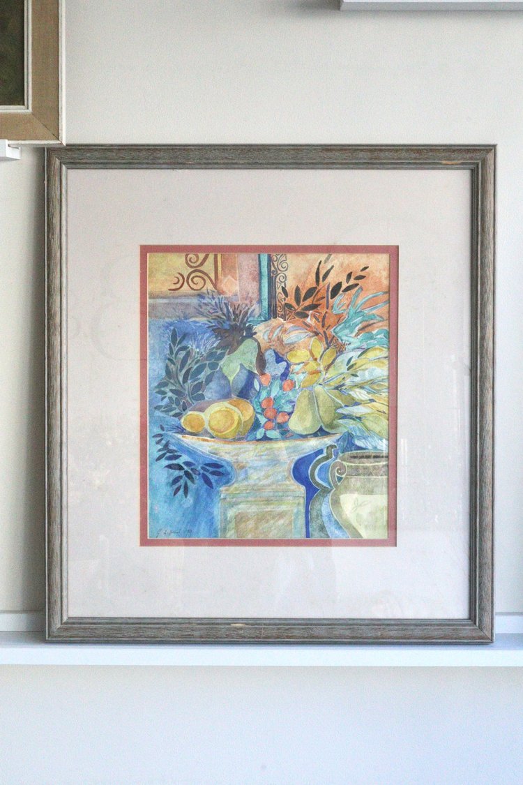 Framed artwork of a still life scene with flowers and fruits on a white wall.