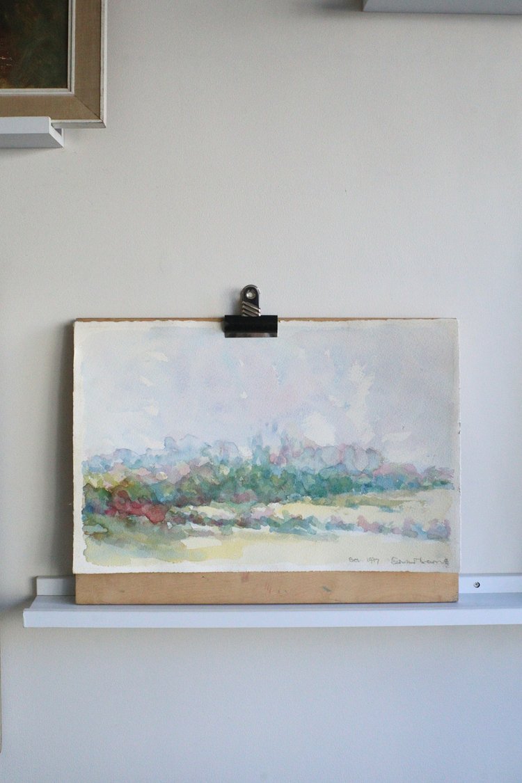 Painting of a landscape on an easel against a white wall