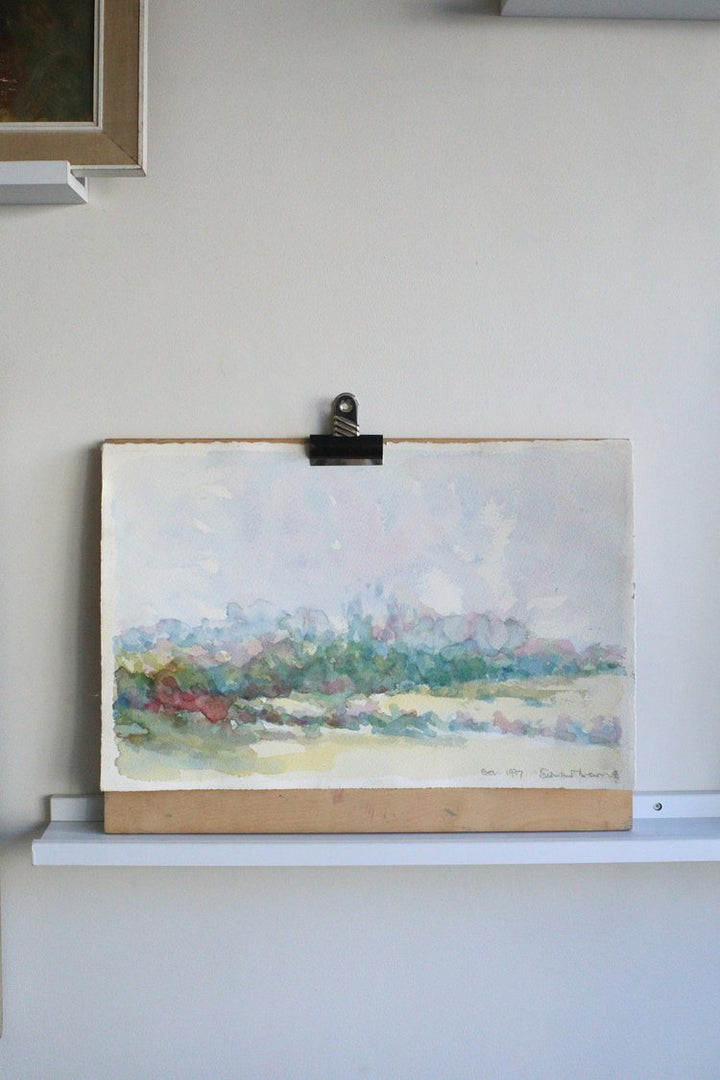Painting of a landscape on an easel against a white wall